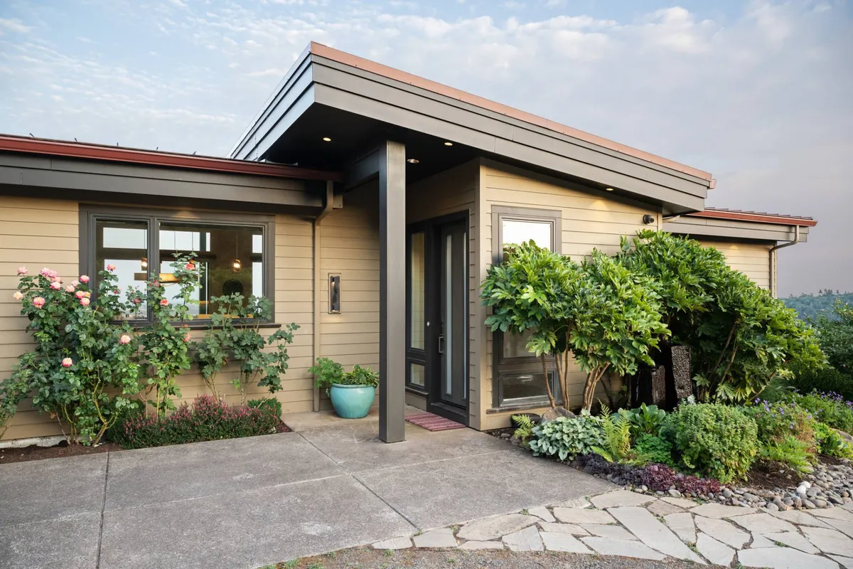 A welcoming view of the home’s front entrance, bordered by a charming landscaped garden and decorative pots, with a clear pathway leading to the porch. The scene exudes hospitality and hints at the beauty of the property’s immediate surroundings.